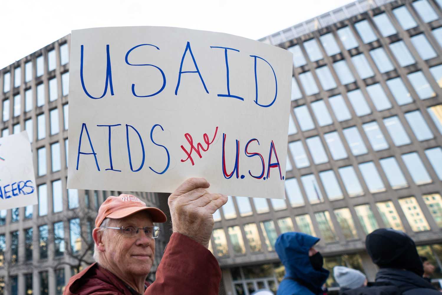 Man holds sign that reads USAID AIDS the USA outside government building