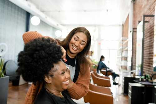 Black, woman hairstylist trimming Black, woman customer's hair at a beauty salon
