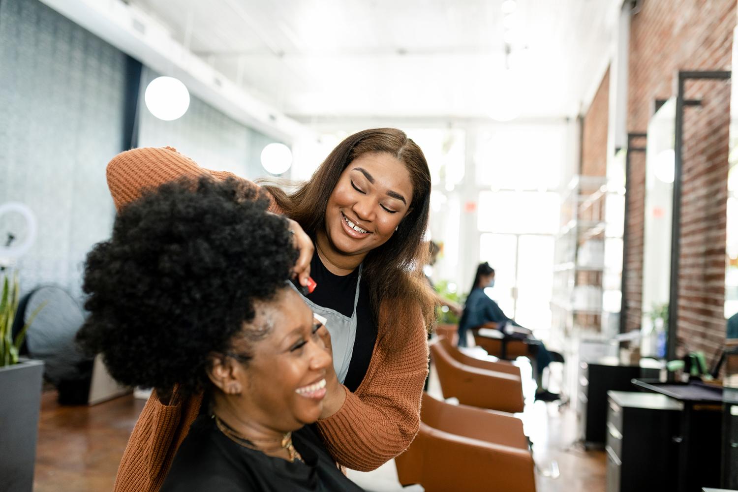 Black, woman hairstylist trimming Black, woman customer's hair at a beauty salon