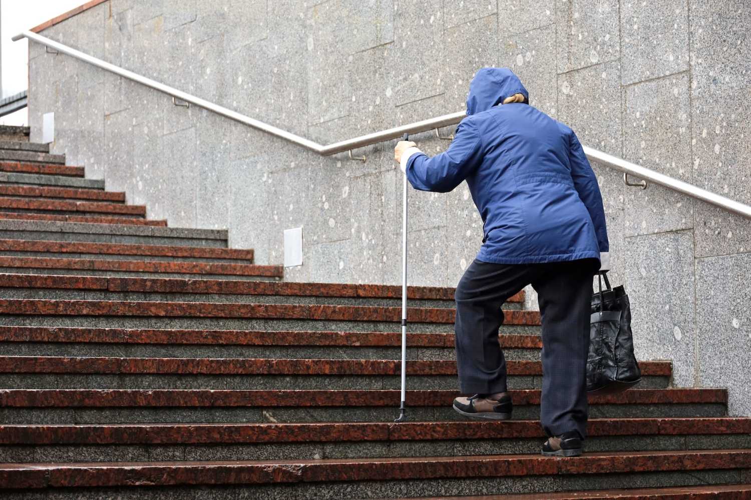 Old woman with walking cane climbing stairs on city street.