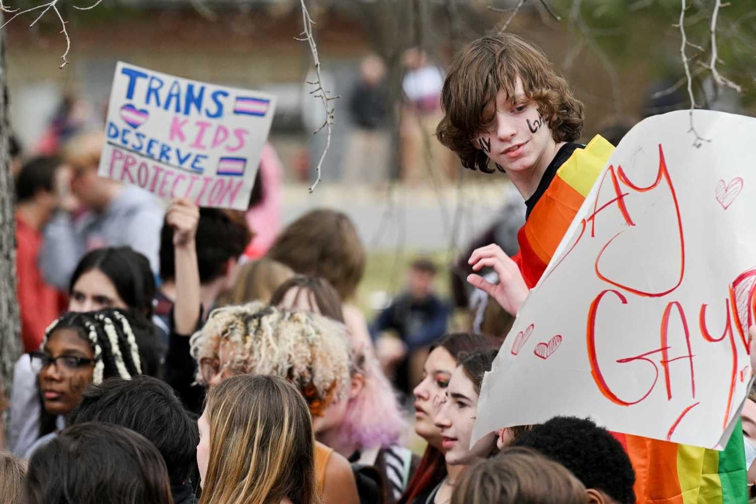 A student wearing a pride flag is handed a "SAY GAY" sign during a walk out to protest proposed education bills at J.M. Atherton High School in Louisville, Kentucky, U.S., February 14, 2023.