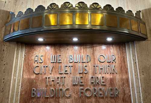 Ornate brass sign that reads "As we build our city let us think that we are building forever"