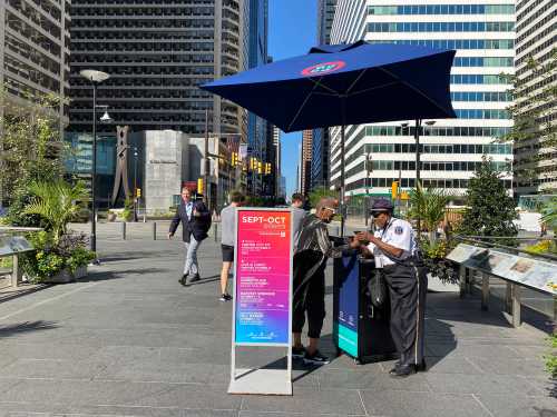 Black female interacts with Black female security officer on the sidewalk in Philadelphia. Skyscrapers and pedestrians in the background
