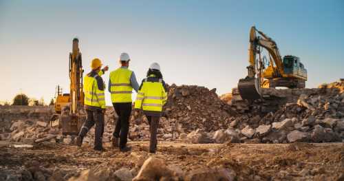 Three workers in safety vests walk though a rocky work site