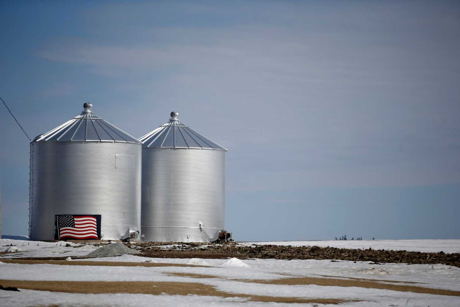 Grain silos with an American flag on the side, in an agricultural field covered in snow