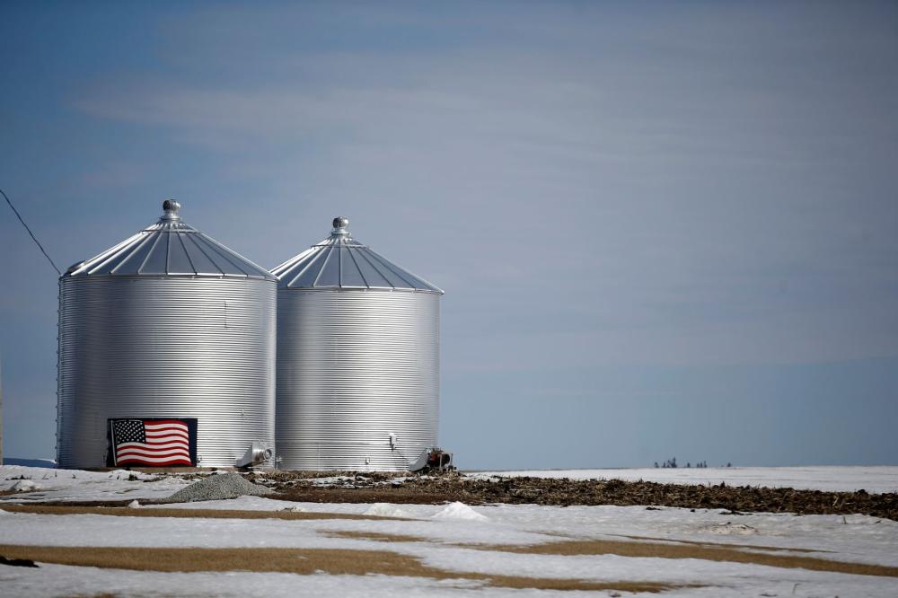 Grain silos with an American flag on the side, in an agricultural field covered in snow