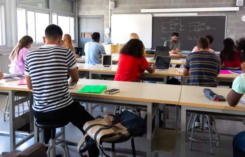 A high school classroom photographed from the back of the room as students study. It looks like they're working on electrical circuits, judging from the chalkboard.