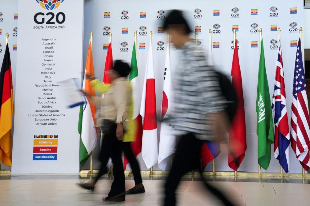 People walk in front of a G20 sign and flags