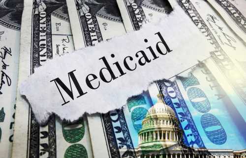 Piece of paper with Medicaid on it on top of 100 dollar bills.