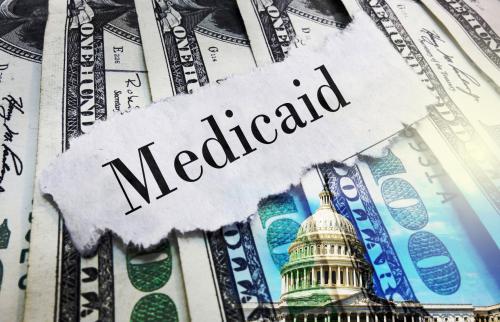 Piece of paper with Medicaid on it on top of 100 dollar bills.