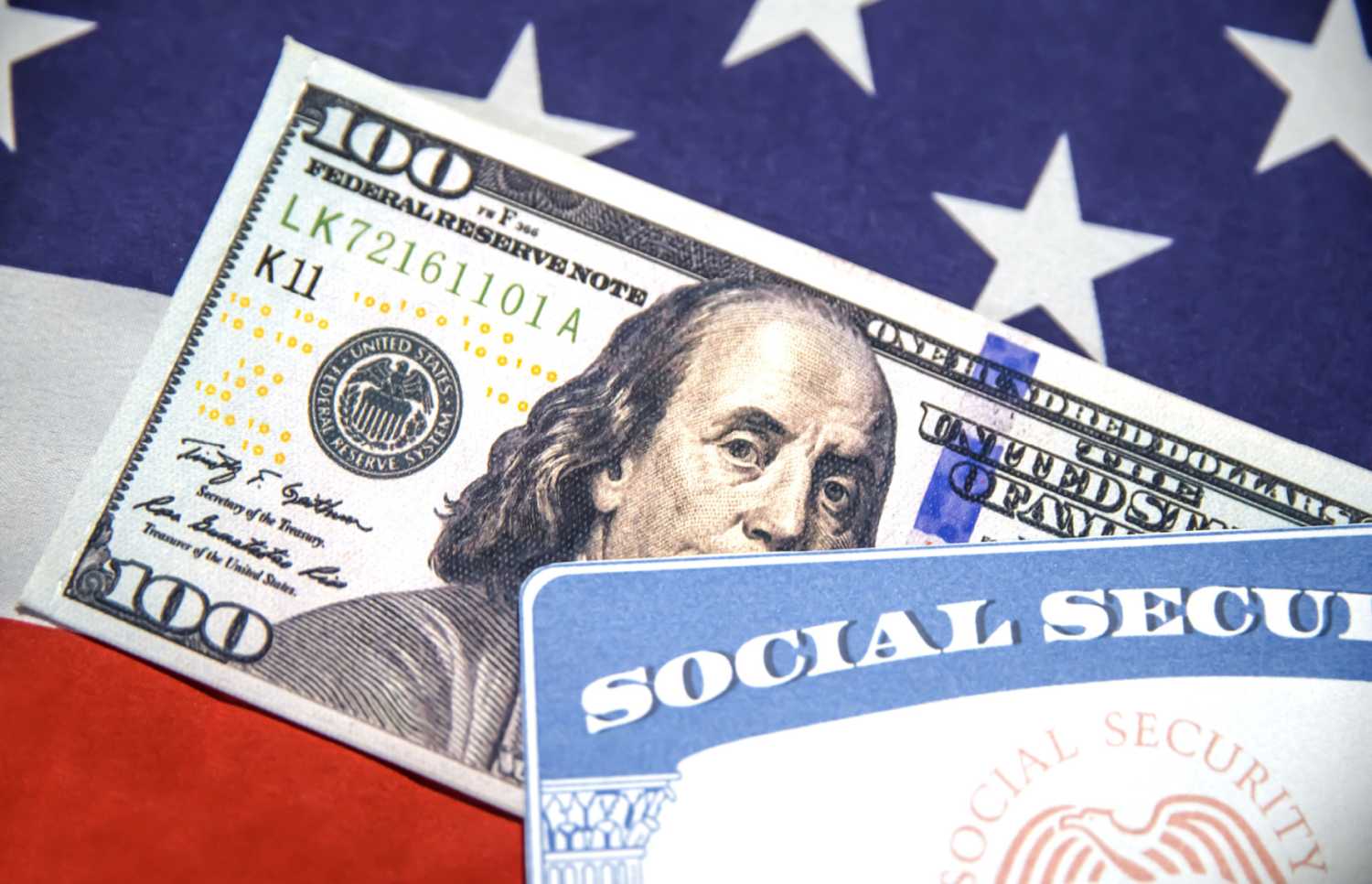 Social Security Card and Hundred dollar bill close-up shot with American flag in the backdrop.