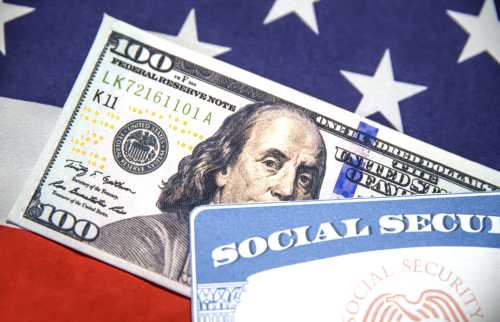 Social Security Card and Hundred dollar bill close-up shot with American flag in the backdrop.