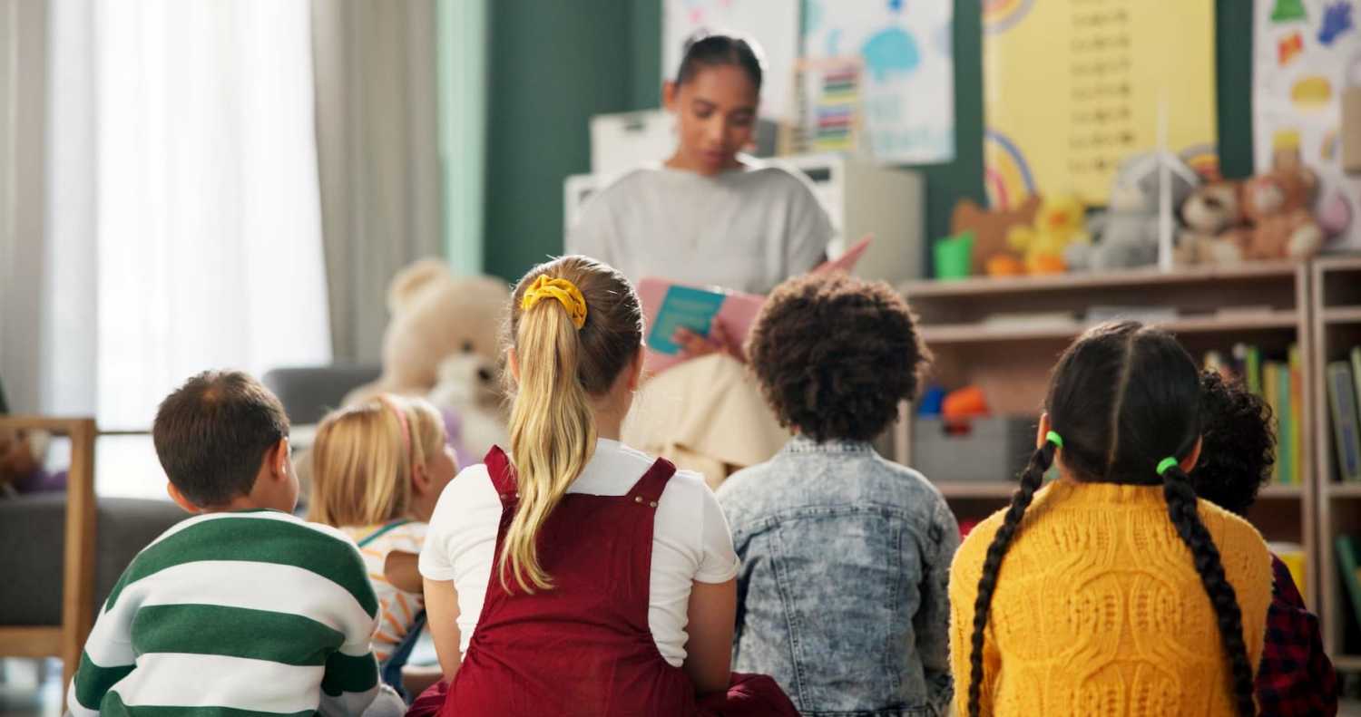 Preschool children and their teacher read a story together in a classroom.