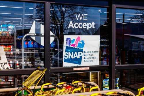 A grocery store window with a sign that says "We accept SNAP - Supplemental Nutrition Assistance Program"