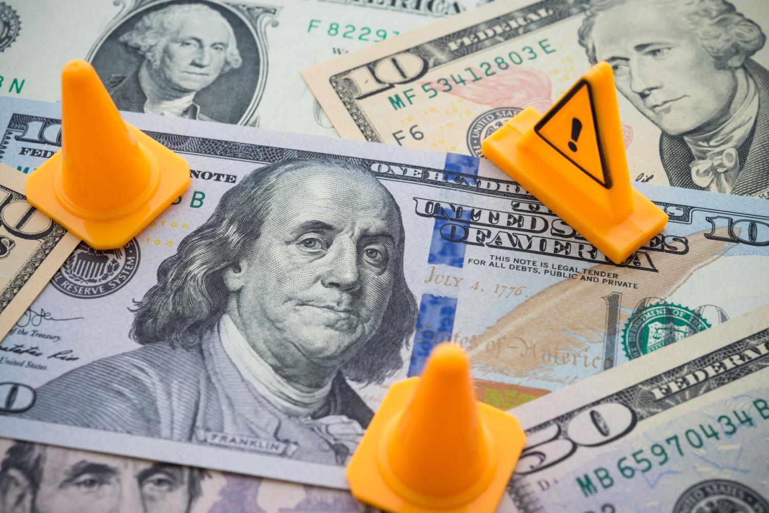 Traffic cones and a caution sign sit upon a pile of U.S. currency