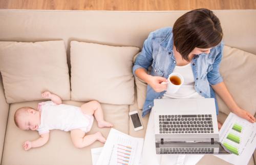 Woman working on her laptop with baby beside her.