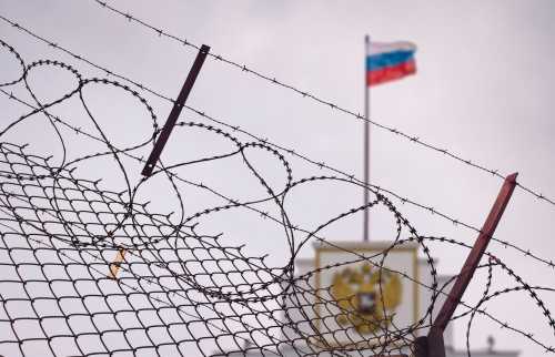 Building with Russian flag behind a barbed wire fence.