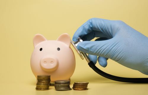 Hand with stethoscope checking a piggy bank.
