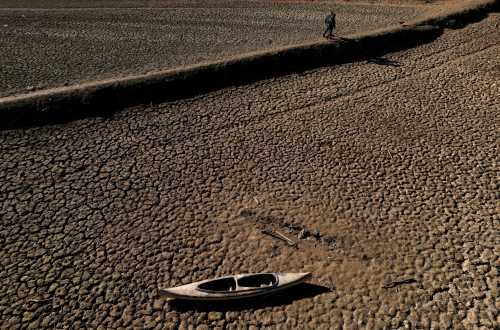 Residents with their dog walk in front of a canoe sitting on a cracked ground at a Sau reservoir, as the Iberian peninsula is at its driest in 1,200 years, in Sant Roma De Sau, Spain, January 31, 2024.