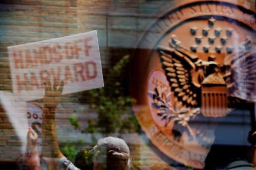 Demonstrators with group Crimson Courage, who gathered to support Harvard University outside a hearing before a federal judge to order U.S. President Donald Trump's administration to restore about $2.5 billion in canceled federal grants and cease efforts to cut off research funding, are reflected in a window of the federal courthouse in Boston, Massachusetts, U.S., on July 21, 2025.