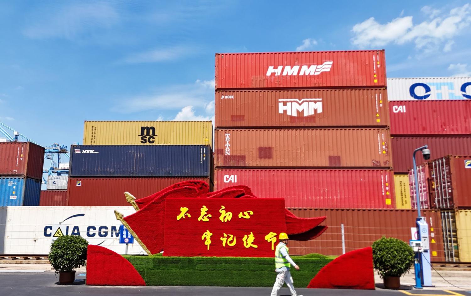 A worker walks past a stack of shipping containers