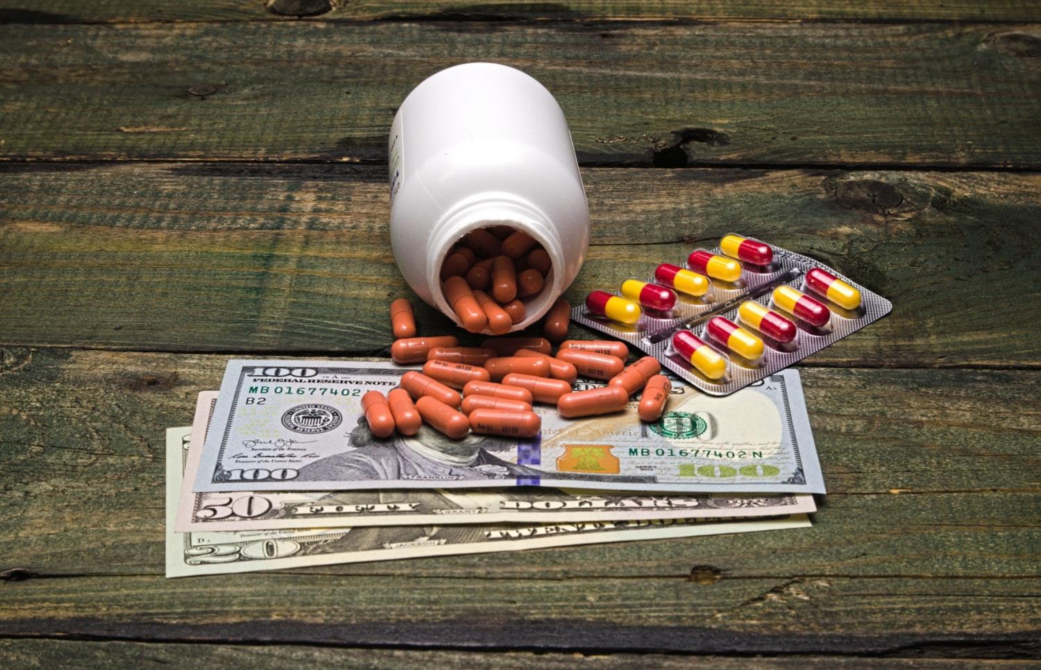 Bottle of pills spilled onto hundred dollar bills.