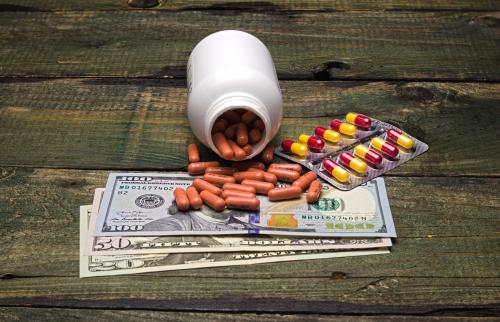 Bottle of pills spilled onto hundred dollar bills.