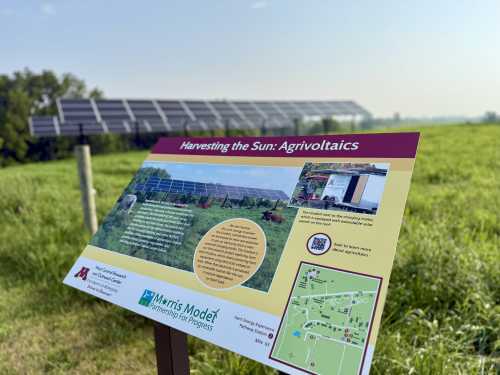 sign reading "Harvesting the Sun: Agrivoltaics," near a solar panel array.