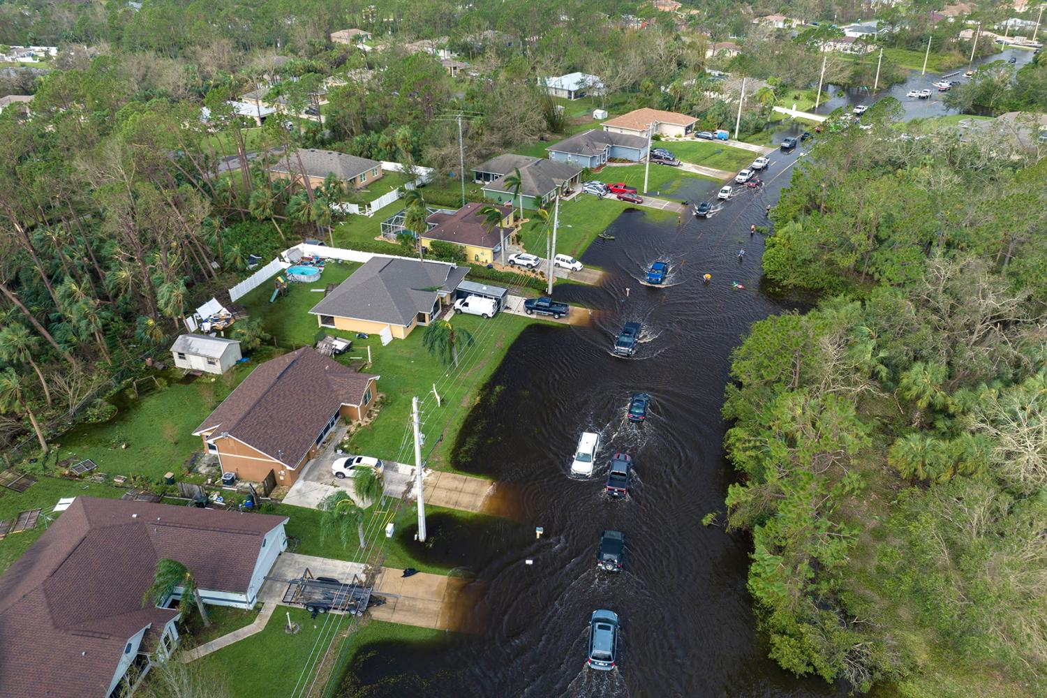 Hurricane rainfall flooded Florida road with evacuating cars and surrounded with water houses in suburban residential area