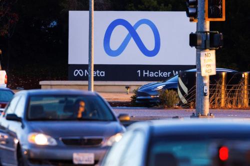 Cars drive in front of a large sign with Meta's logo, a blue infinity sign.