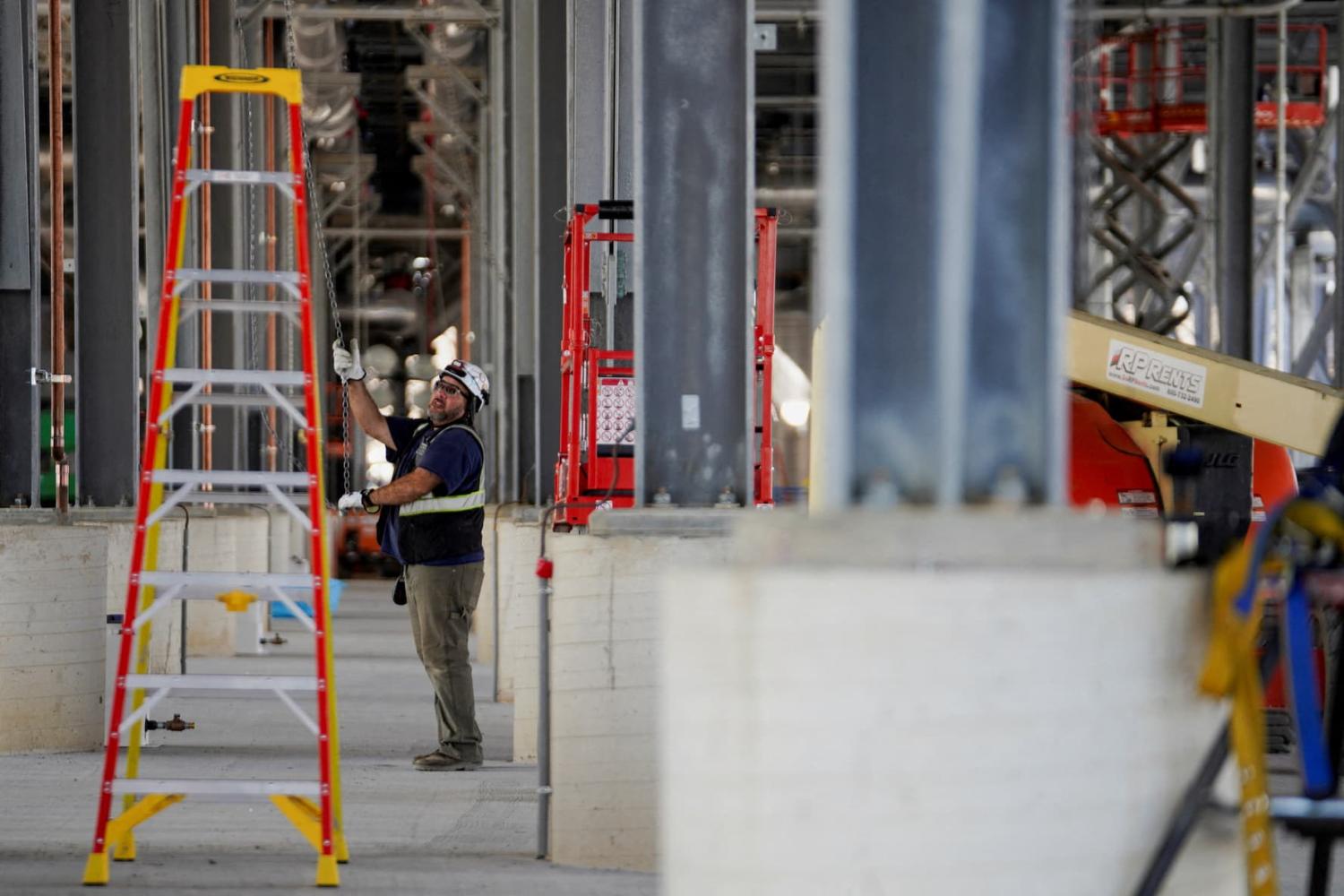 A person working on the construction site of a data center, with scaffolding, a ladder, and equipment in the fore and background.