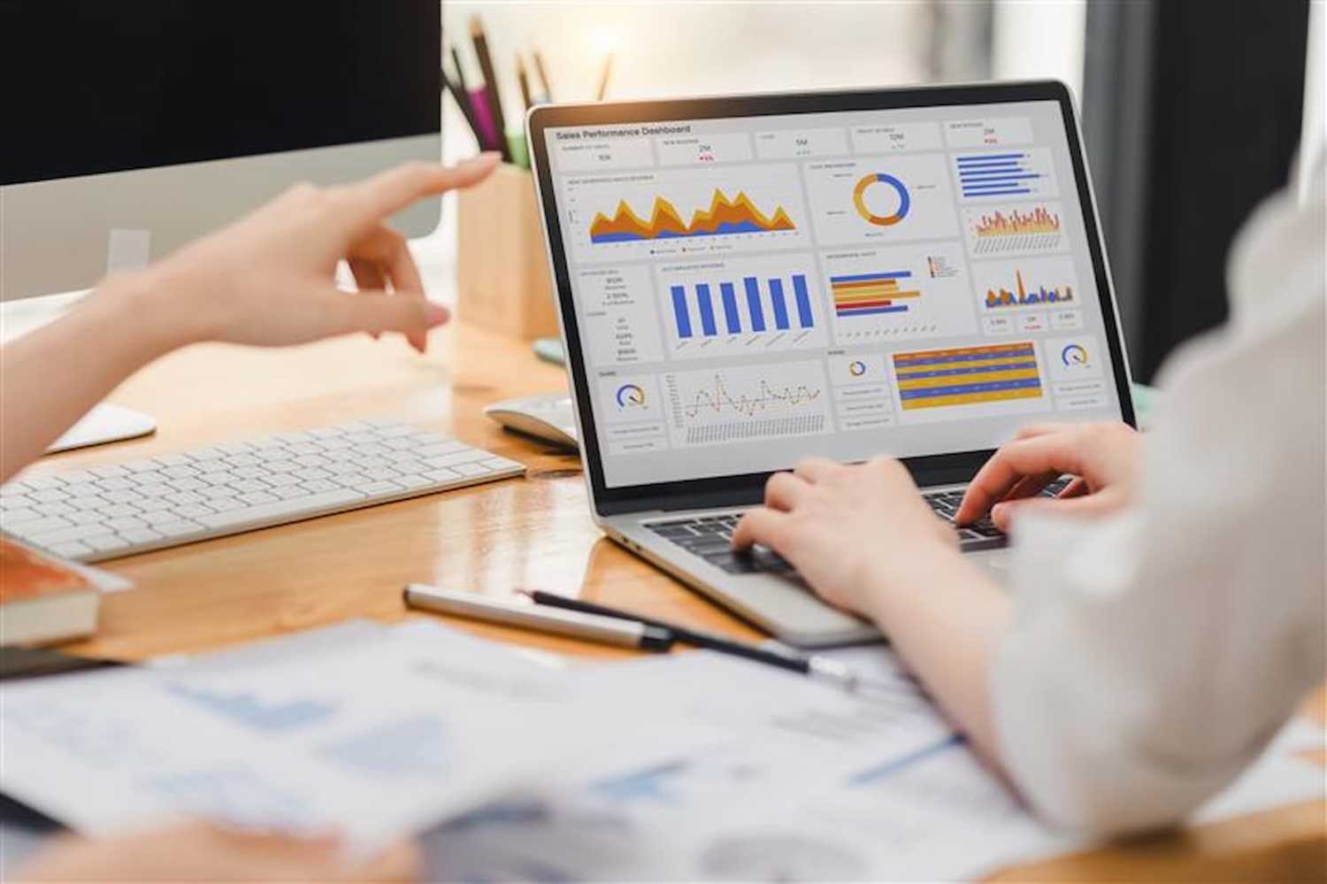 Two businesspeople reviewing charts, graphs, and a dashboard on a laptop in an office while preparing a financial report