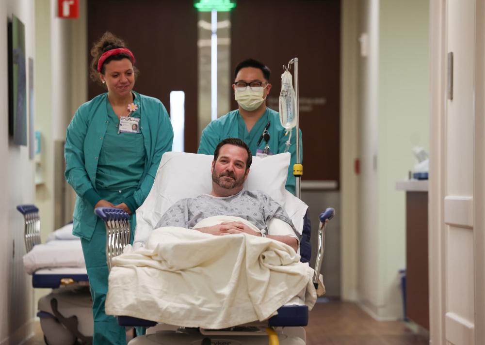 Nurses Jenny Arcaro, left, and Mike Marasigan guide patient Mike Lowe to a procedure room at Northwestern Lake Forest Hospital on April 18, 2025.