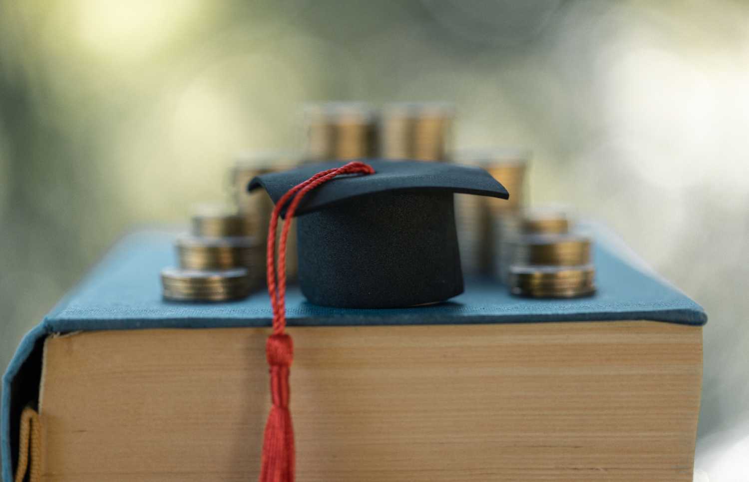 Graduation cap and coins on top of a textbook.
