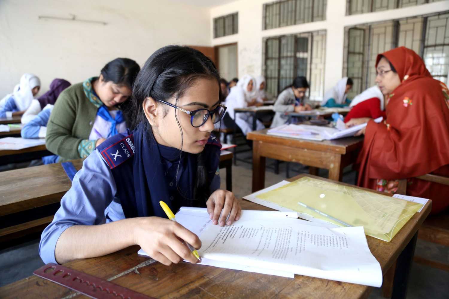 A girl looks at exam papers while sitting at a desk in a classroom