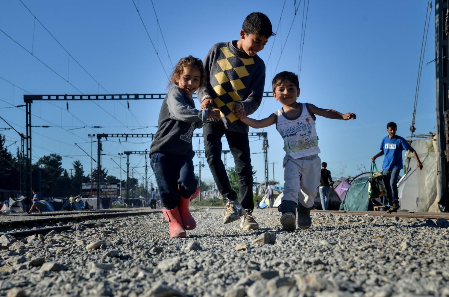 Children play near train tracks against a background of tents
