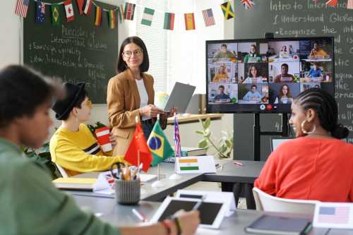 Students and a teacher in a classroom with a videoconference screen