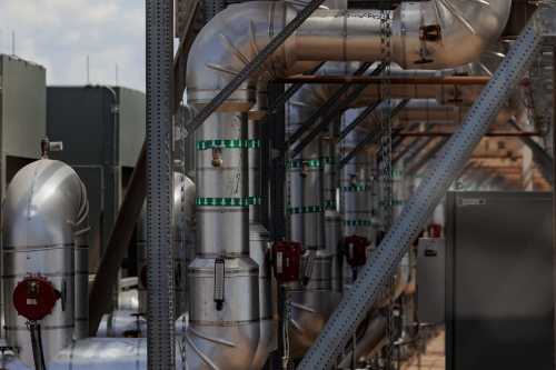 A photo of many large pipes feeding from one side of the picture to the other. The sky and other parts of a data center can be seen in the background.