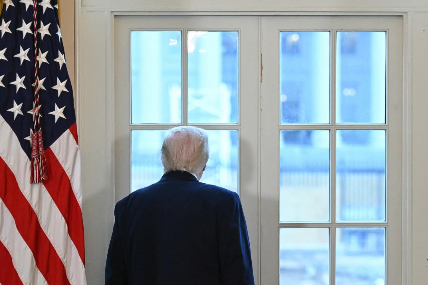 President Donald Trump looks through a window of the White House