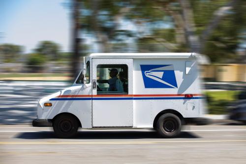 A USPS mail truck driving on a road.