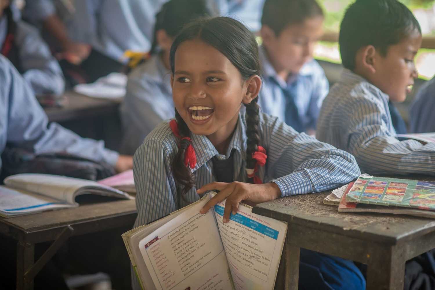 A young girl smiles when holding a schoolbook in the classroom