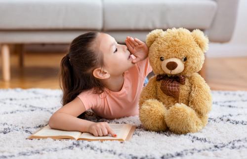 A girl whispers into the ear of a teddy bear