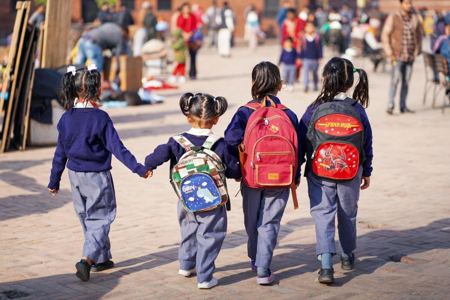 Young children wearing backpacks and school uniforms walk while holding hands