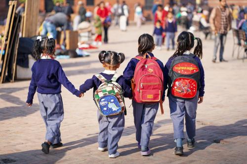Young children wearing backpacks and school uniforms walk while holding hands