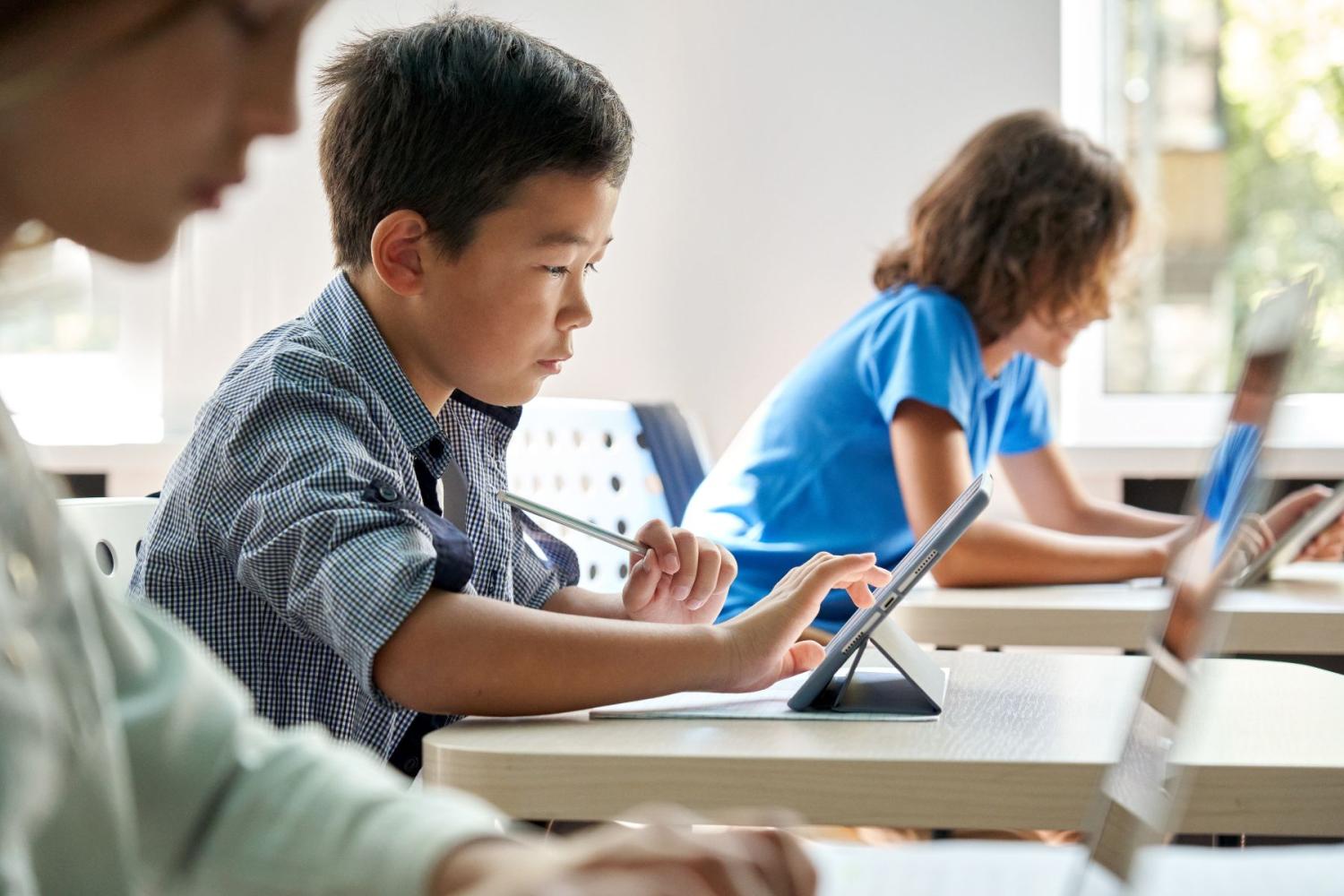 Children use tablets while sitting at desks in a classroom