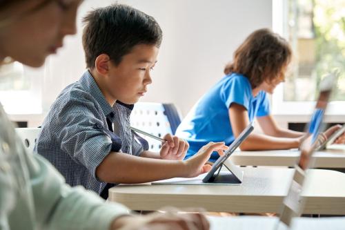 Children use tablets while sitting at desks in a classroom