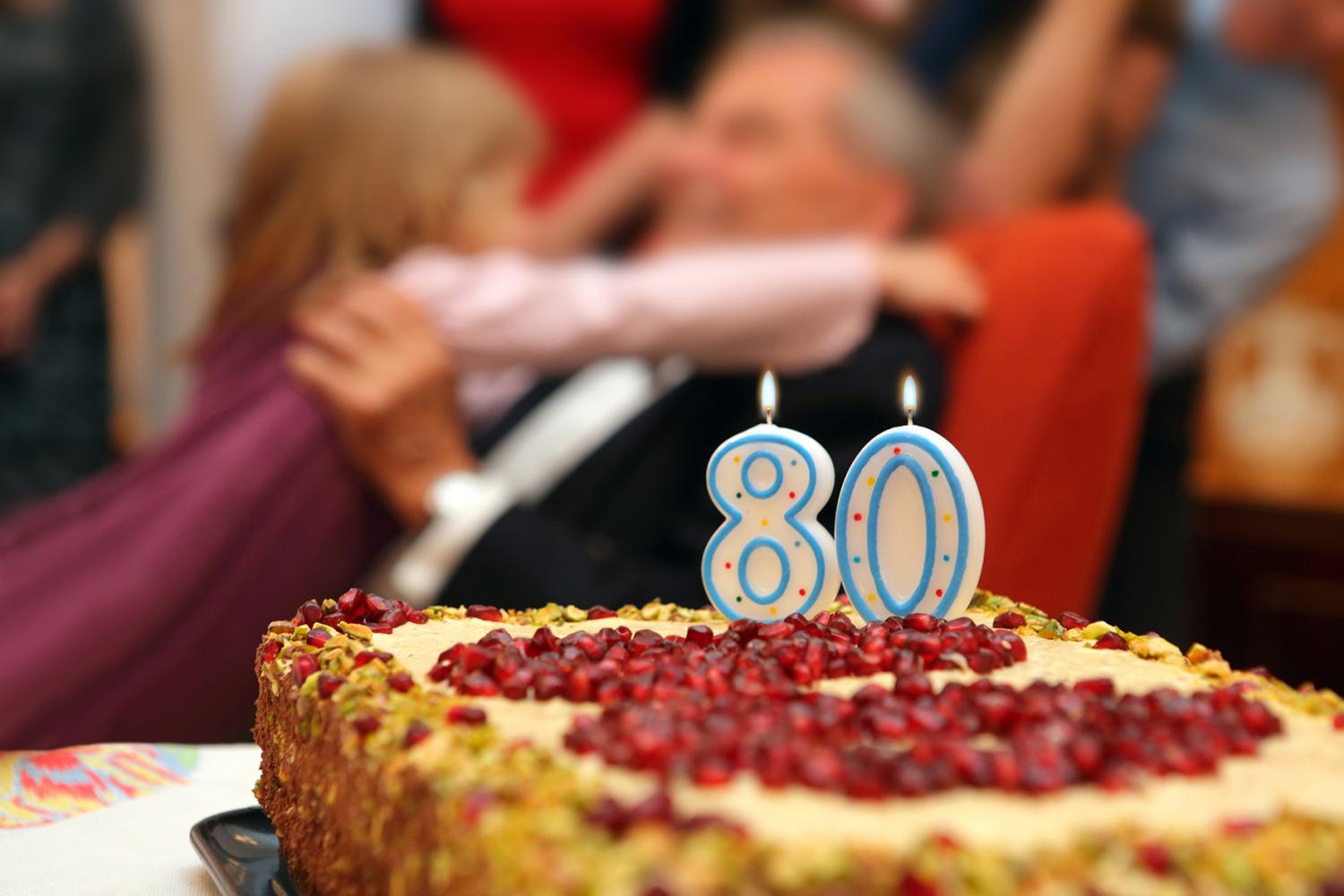 Eightieth birthday Grandfather with granddaughter and family with number 80 on cake.