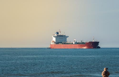 A person watching an oil tanker from the shore.