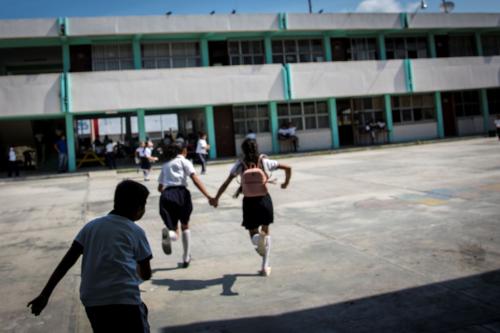 Children in school uniforms hold hands while running toward their school