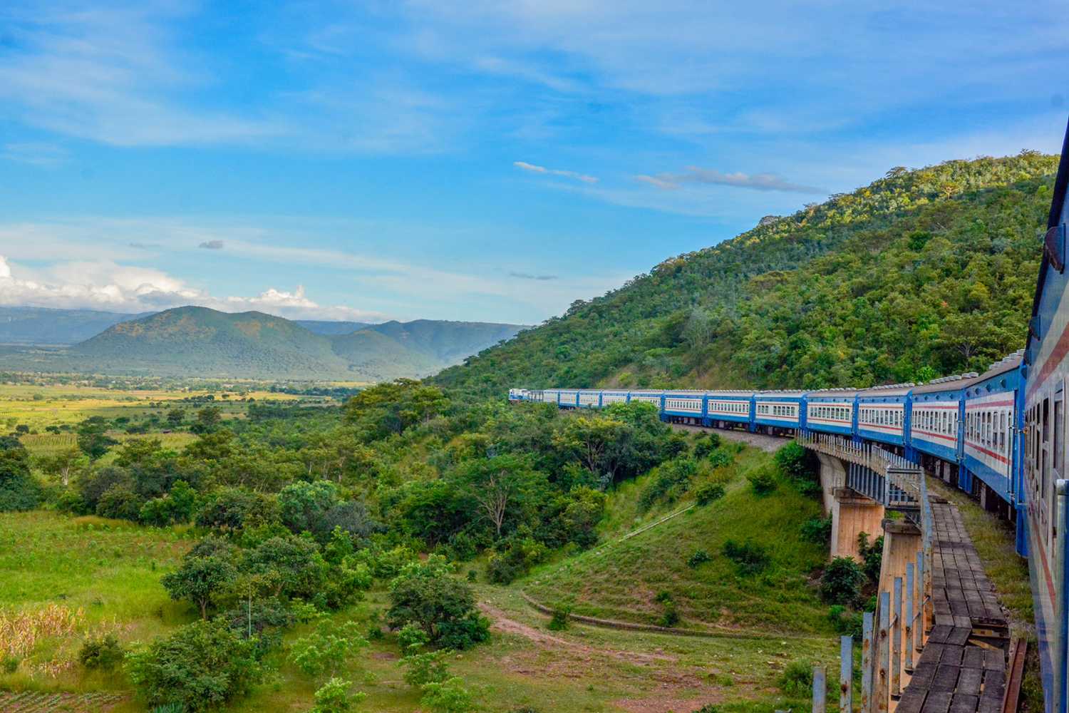 A blue train travels through green mountains